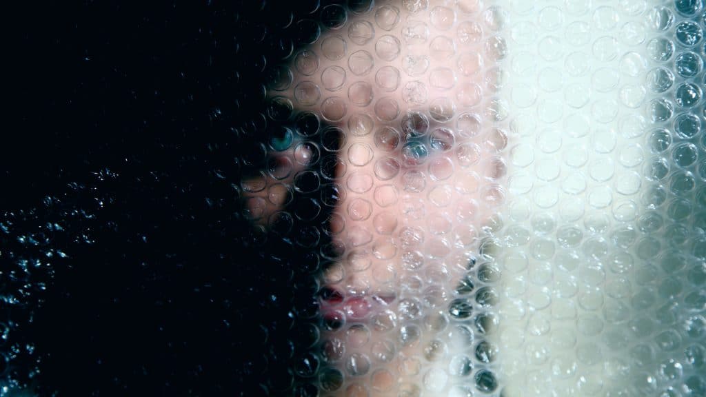 Portrait of a young woman obscured behind plastic bubble wrap.